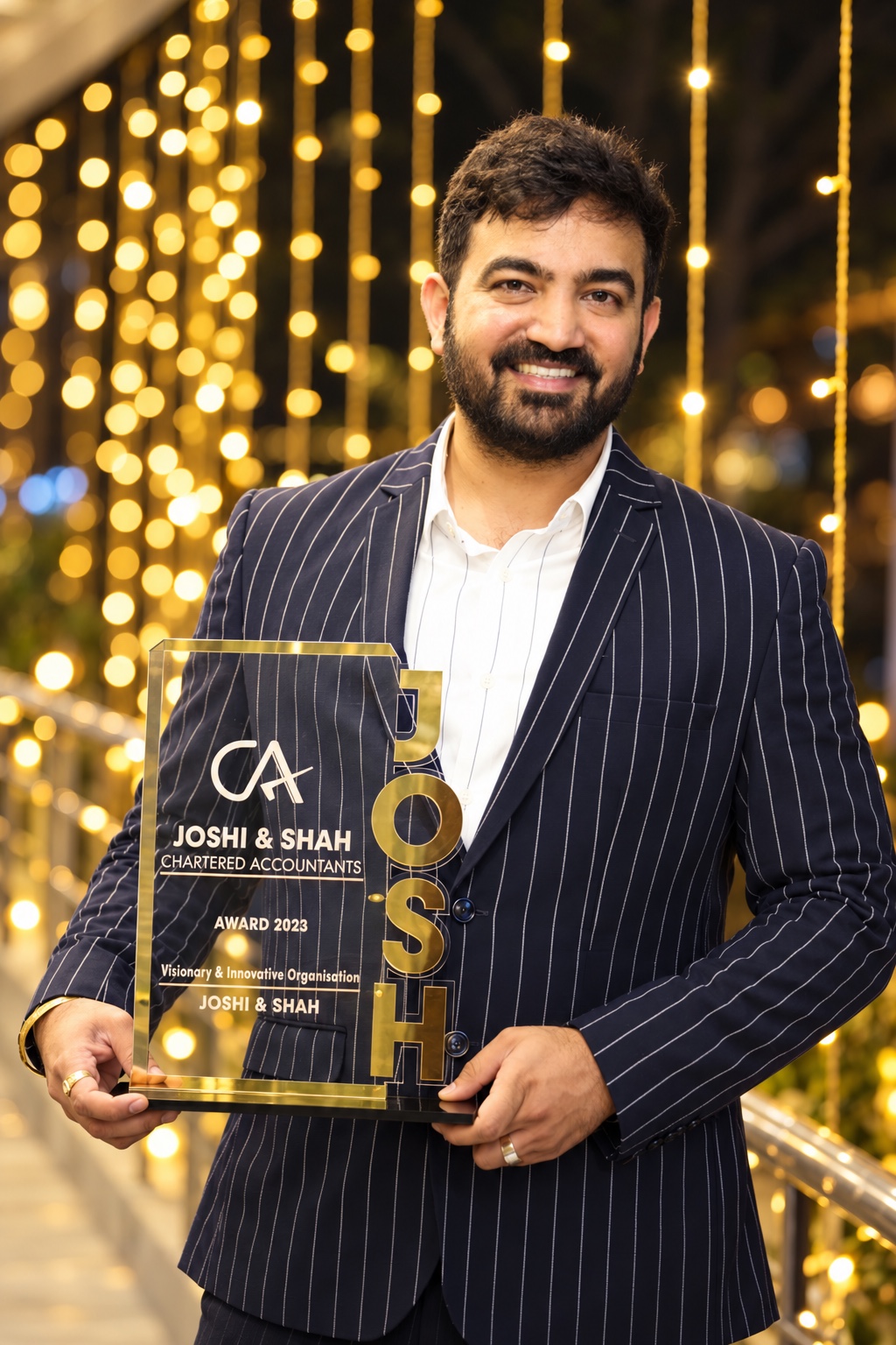Jigarkumar Shah in a pinstripe blazer holding a Joshi & Shah award